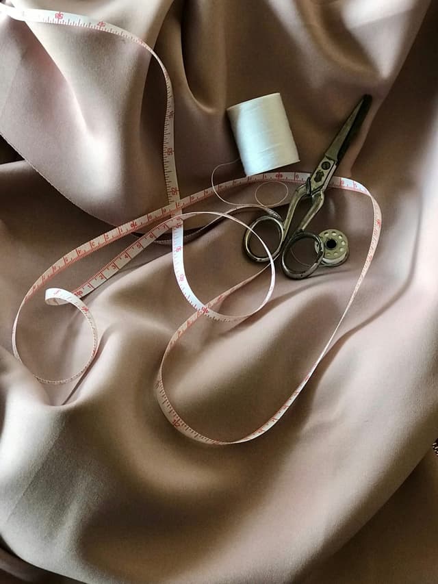 Measuring tape, thread and tailoring scissors on soft fabric