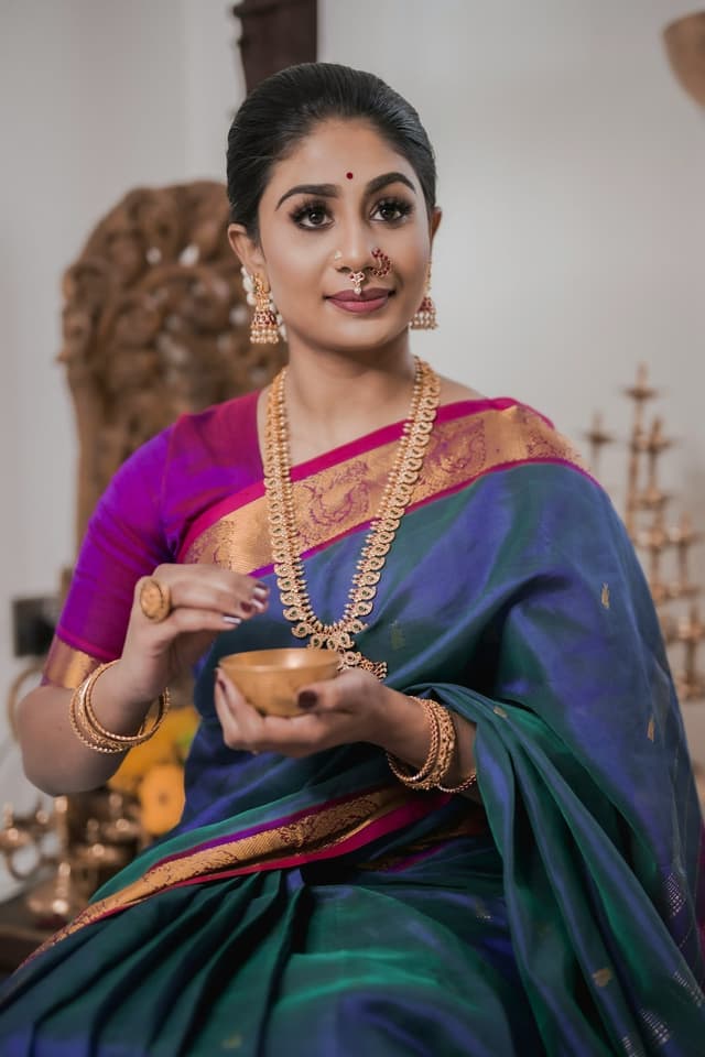 Woman in a teal and blue Kanjeevaram silk saree with a gold zari border and gold jewellery